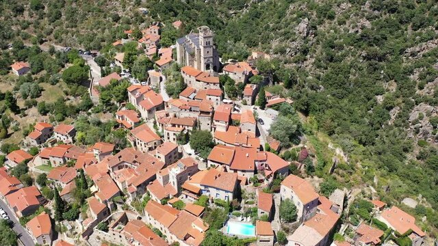 General summer view of picturesque French village of Eus in natural region of Conflent with tightly grouped houses, medieval church and castle ruins on top of hill