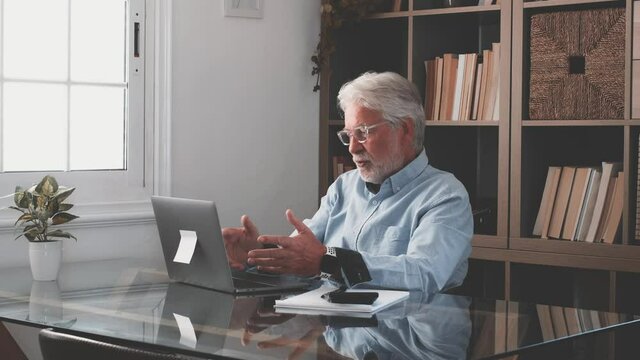 Happy old caucasian businessman smiling working online watching webinar podcast on laptop and learning education course conference calling make notes sit at work desk, elearning concept
