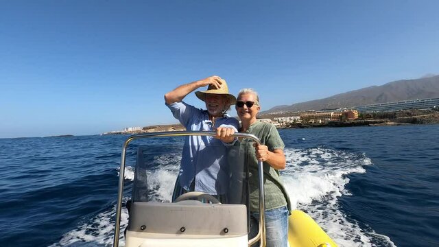 Beautiful and cute couple of seniors or old people in the middle of the sea driving and discovering new places with small boat. Mature woman holding a phone and taking a selfie with hew husband
