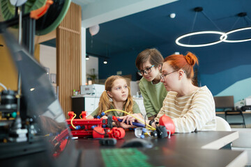 Portrait of two children building robot during engineering class at school with female teacher helping , copy space