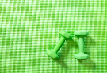 Top view, 2 green dumbbells flat lay on yoga mat, set of indoor exercise equipment. Lifestyle workout at home. Monochromatic color objects on pattern texture with copy space. Wellness, healthy concept