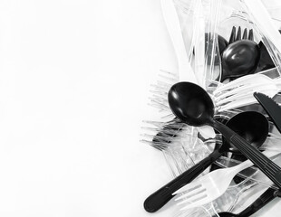 Pile of clean plastic takeaway cutlery on table (spoon, fork, knife). Reusable or recycle utensil in minimal, contrast and monotone concept (black, white, clear color collection) with negative space.
