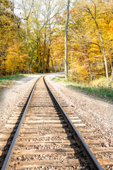 Obraz premium Beautiful scenery of countryside railway track with yellow forest, depth of field. Rural transportation by train, nature route journey in sunny day. Colorful landscape background of travel.