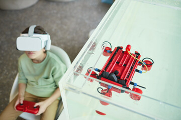 High angle portrait of boy wearing VR headset while operating robotic boat in school laboratory, copy space