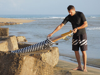 Man pulls out a surfboard from cover in the beach.