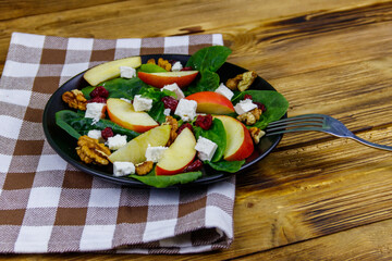 Autumn spinach salad with apple, feta cheese, walnut and dried cranberry on wooden table. Healthy vegetarian food