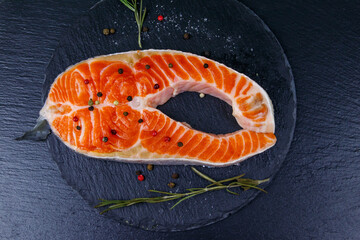 Raw salmon steak with spices on black slate. Top view
