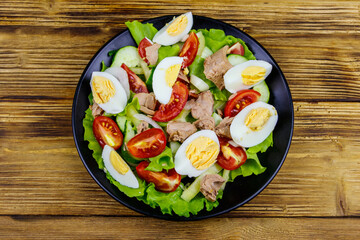 Tasty tuna salad with eggs, lettuce and fresh vegetables on wooden table. Top view