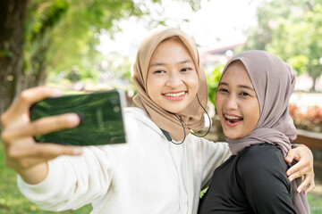 two happy muslim friend taking selfie or video calling outdoor using her smart phone during sport break outdoor