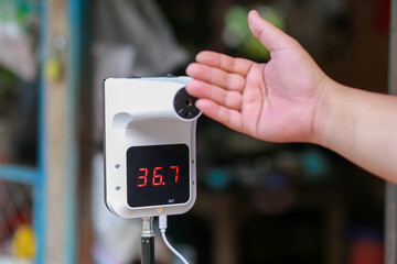 A fever meter with a stand and a man's hand is measuring fever in public areas