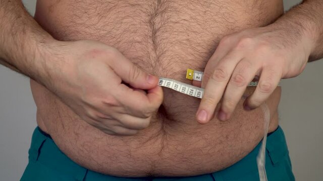 fat man measures the size of the abdomen with a centimeter measuring tape. Losing Weight Day. people suffer from excess weight. 