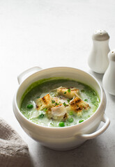 Broccoli and green peas soup-puree in white bowl close up
