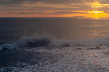 Beautiful view of the ocean waves chasing in rocks with a magical sunset in the horizon
