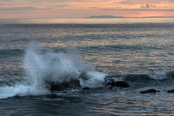 Beautiful view of the ocean waves chasing in rocks with a magical sunset in the horizon
