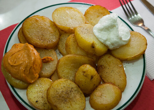 Traditional Spanish fried potatoes Patatas bravas served with cheese sauce and spicy sauce with paprika and chili. High quality photo