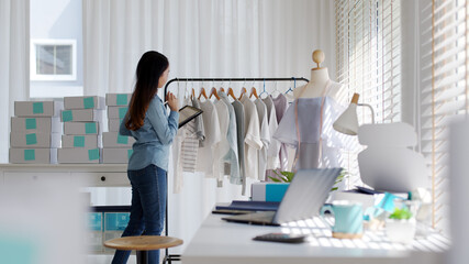 Young attractive beautiful hipster asia female fashion store owner use digital tablet check stock clothes or package box on rail rack at home office small SME business entrepreneur e-commerce concept.