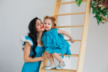 A woman with a little girl in beautiful blue dresses in a bright studio decorated with flowers....