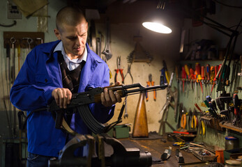 Fototapeta na wymiar Gunsmith with Kalashnikov assault rifle in a weapons workshop
