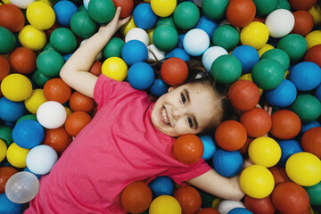 a child in the children's playroom. The girl is having fun among the colorful balls. Dry Pool Party