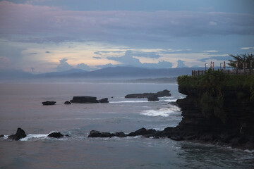 Incredibly beautiful sunset by the ocean in Bali. The bright sun sets in the water. The rays of the sun peeping out from behind the clouds and a beautiful reflection of the sunset in the water