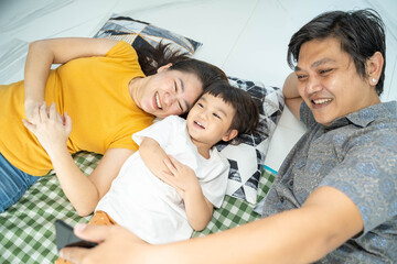 Family and technology concept, Asian happy family lie down on the floor having fun while using smartphone and taking or video call with family.