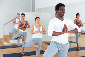 Young men and women maintaining healthy lifestyle practicing yoga on mats in dance studio