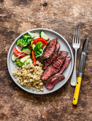 Delicious lunch - bulgur, fresh vegetable salad and steak on a wooden background, top view
