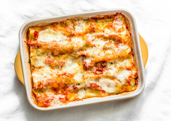 Cannelloni with spinach and ricotta baked with tomato sauce and mozzarella on a light background, top view