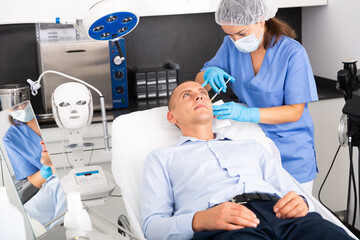 Obraz premium Skilled woman beautician filling males wrinkles using rejuvenating injections in clinic of aesthetic medicine