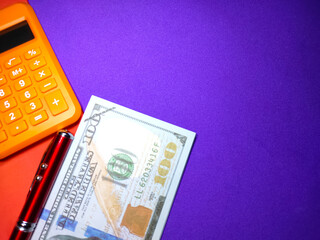 Selective focus of dollar banknote,calculator and pen on purple background with copy space.