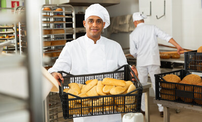 man in chefs uniform with bread in tray in bakery