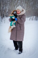 Portrait of an elderly woman with a dog. Woman with pekingese dog walking on the snowy field.
