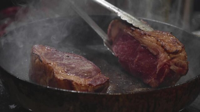 Beef steak being fried on frying pan. Steam flow up from the steak. Close up slow motion shot.