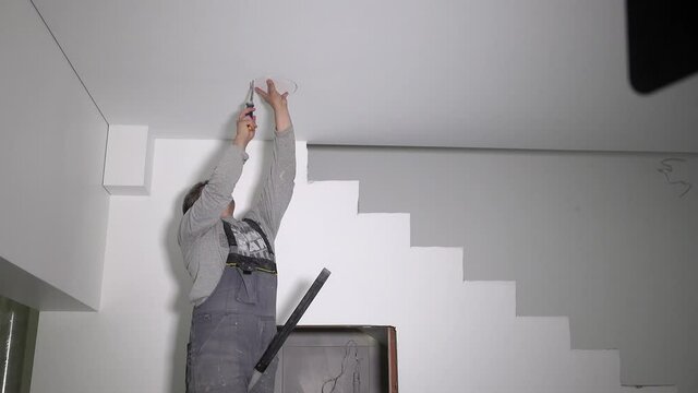 Male worker with handsaw cut hole in drywall ceiling for led light panel