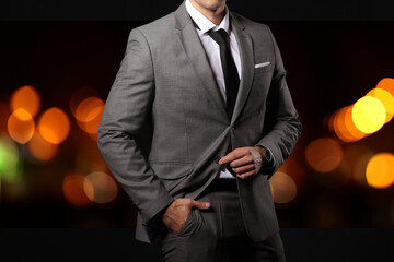 Handsome young man in elegant suit on dark background with blurred lights