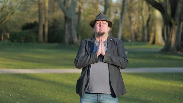 [4k] best ager goatee man wearing hat praying to god in park