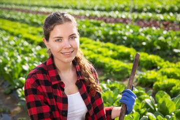 Portrait of smiling young girl working on vegetable beds in small farm on sunny spring day ..