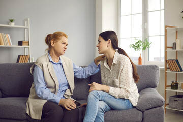 Naklejka na ściany i meble Senior mother and young grown-up daughter talking sitting on sofa at home. Wise mom supporting daughter and giving her life and relationship advice. Family, mutual understanding, helping each other