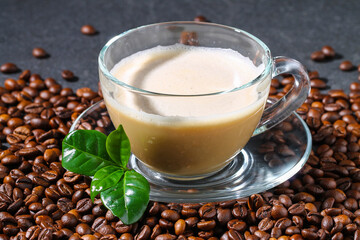 Cup of coffee on a gray table with coffee beans and coffee leaves. Closeup.