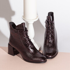 Pair of new black women short boots on medium high heels on beige background studio shot