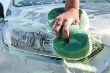 Female hand using sponge with soap foam cleaning her car