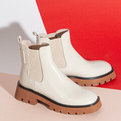 Pair of new white women short boots on medium high heels on beige background studio shot