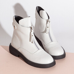 Pair of new white women short boots on medium high heels on beige background studio shot