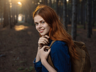 Side view of a woman in a blue shirt in a pine forest with a backpack on her back