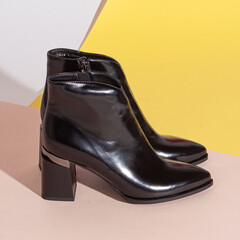 Pair of new black women short boots on medium high heels on beige background studio shot