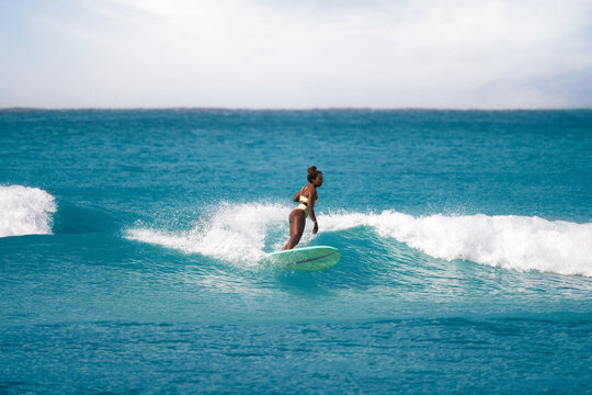 Charming curly African-American dark-skinned young woman, professional surfer do noseride on a long surfboard 