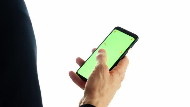 Chroma Key Green screen phone with tracking markers. Over the shoulder shot of businessman holding mobile isolated on white background, scrolling gestures, watching content. Mock-Up, Close-up 4k