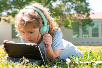 Online kids education. Portrait of cute smart clever school boy nerd doing homework in shool park.