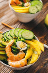 Bowl of fresh salad with mango, shrimps and vegetables on wooden background