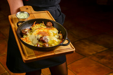 Grilled sausages from barbecue grill with melted cheese on a frying pan served by waiter in restaurant or diner.